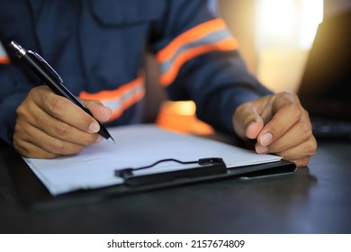 An industrial or shipping inspector auditor supervisor in a reflective jacket is writing a pen on a clipboard to check the inventory of tasks that need to be done.