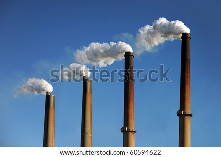 Industrial smokestacks with smoke clouds over blue sky