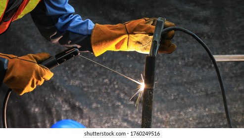 Industrial technician engineer in blue protective cloth wear safety mask, helmet, glasses welding metal. professional welder man welding steel structure with fire spark in factory. selective focus.
