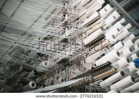 Industrial textile machine weaving polypropylene yarn from multiple spools on a creel, manufacturing fabric material