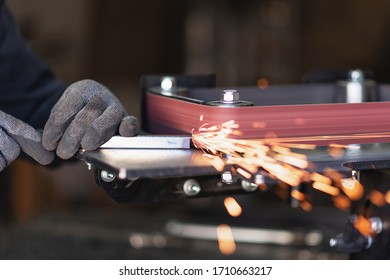 Industrial tool worker grinds a square steel pipe on a rotating belt sander - Powered by Shutterstock