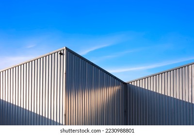 Industrial Warehouse Building with Metal Corrugated Steel Exterior Wall and Geometric Aluminium Roof with Light and Shadow on Surface against Blue Sky Background, Low Angle view - Powered by Shutterstock