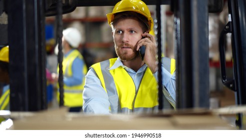 Industrial warehouse manager sitting in forklift truck and having phone call. Portrait of handsome forklift driver having mobile phone conversation in factory storehouse - Powered by Shutterstock