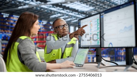 An Industrial Warehouse Worker Uses Multiple Computers To Manage Inventory And Parcels