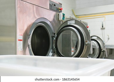 Industrial washing machine are turning off, front doors are left open while laundry trolly cart is on the front. Shot taken in the factory. Selective focus on the front door of washing machine.  - Powered by Shutterstock