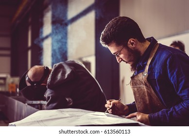 Industrial Welder checking blueprint in the background welder welding metal profiles - Powered by Shutterstock