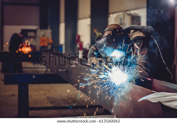 Industrial Welder With Torch and Protective\
Helmet in big hall welding metal\
profiles