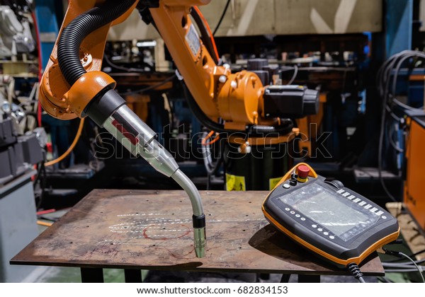Industrial welding robots and remote\
control at test table area in manufacturer\
factory