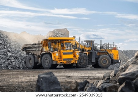 Industrial wheel loader loading ore to big yellow mining truck. Banner Open pit mine industry.