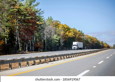 Industrial White Day Cab Powerful Big Rig Semi Truck Tractor Transporting Cargo In Container Trailer Running On The Divided Highway With Autumn Maples Trees Line In New Hampshire New England