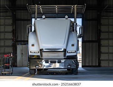 Industrial white possibly broken big rig semi truck with open hood standing in mechanical workshop for repair after technical diagnostics inspection and periodic maintenance procedure