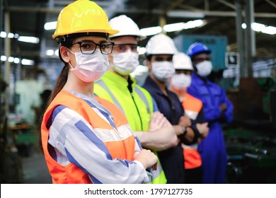 Industrial woman engineer or factory worker wearing helmet and hygiene face mask with teamwork stand in line at manufacturing plant.People working industry during covid pandemic.