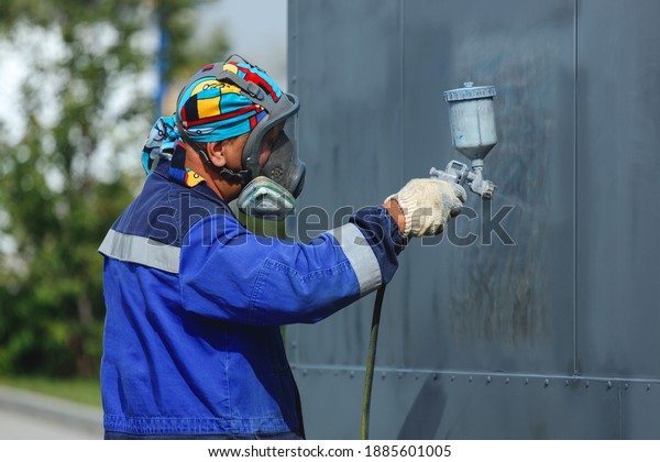 Industrial work.\
Priming of metal products from the compressor gun. A worker in\
overalls and a protective mask paints the body of a truck trailer\
or a metal car. Not staged\
photo