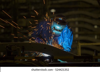 Industrial Worker At Assembly Line In Car Factory Is Welding Automotive Part
