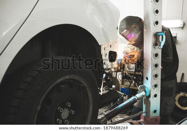 Industrial worker at car service\
welds automotive body. Metalworking with carbon dioxide\
welding.