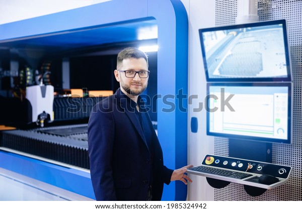 Industrial worker entering data in\
CNC laser turning machine at automatic modern factory\
floor.