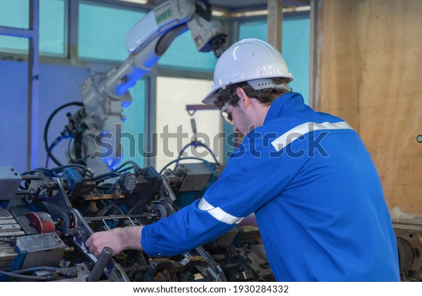 Industrial worker on quality control using steel\
measuring tape measure length a part of an operation machine at\
factory site with the smart robot welding hand system automated\
manufacturing\
machine.