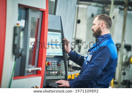 Industrial worker operating cnc machine at metal machining industry
