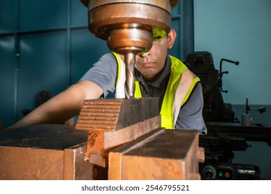 An industrial worker operating a drill press in a workshop. The focus is on the precision and concentration required to handle machinery. The worker wears a safety vest, ensuring a secure work. - Powered by Shutterstock