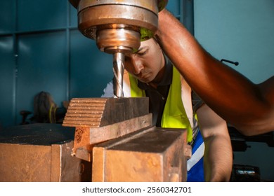 An industrial worker operating a drill press in a workshop. The focus is on the precision and concentration required to handle machinery. The worker wears a safety vest, ensuring a secure work. - Powered by Shutterstock