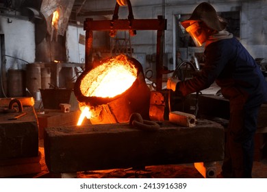 Industrial worker in protective gear pours molten metal at steel foundry. Manufacturing process in heavy industry with furnace. Skilled laborer handles high-temperature metallurgy, safety action. - Powered by Shutterstock