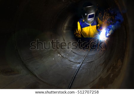 Industrial worker welding metal and many sharp sparks inside piping construction with confined space .
