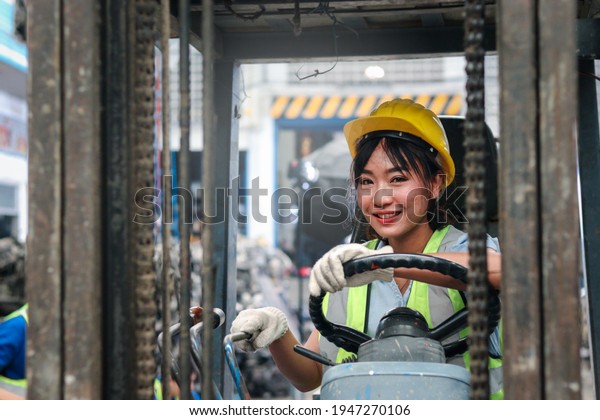 Industrial worker\
woman wearing helmet driving forklift car at manufacturing plant\
factory industry, Asian beautiful female engineer and many engine\
parts as blurred\
background
