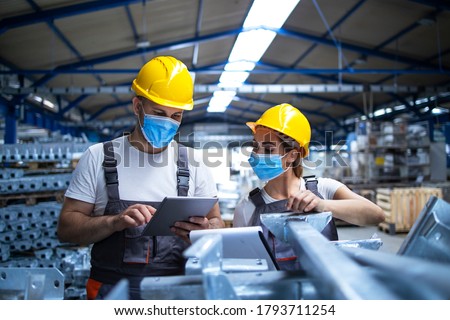 Industrial workers with face masks protected against corona virus discussing about production in factory. People working during COVID-19 pandemic.