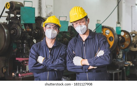 Industrial workers wearing masks in their uniforms and crossed their arms inside a metalwork factory. - Shutterstock ID 1831127908