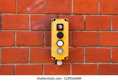 Industrial Yellow Switch Box With Power On And Off Switches Buttons And Key Lock Installed Outdoors On A Red Brick Wall From Warehouse. 