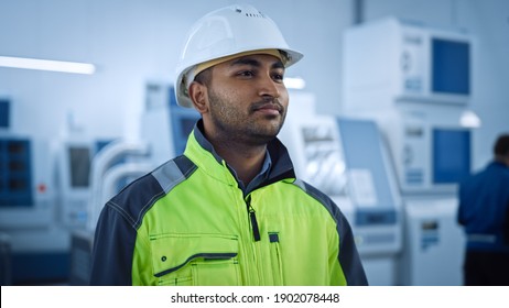 Industry 4 Factory: Portrait of a Modern Worker Wearing Safety Jacket and Hard Hat Walks Through Contemporary Industrial Workshop where Professionals are Working and Programming CNC Machinery