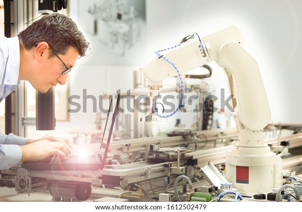 Industry 4.0 concept; Close-up of an\
Engineer who is working on laptop to program robot arm and smart\
factory automation during automated car on production line is\
waiting. smart\
manufacturing.
