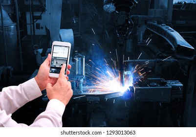 Industry 4.0 ,  Concept  Of Man Hand Holding Cell Phone Or Tablet With Augmented Reality Screen Software And Blue Tone Of Automate Wireless Robot Arm In Smart Factory Background. Mixed Media