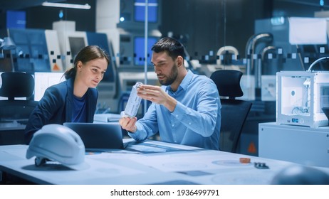 Industry 4.0 Modern Factory Meeting Room: Chief Engineer Holds Mechanism, Shows It To Female Designer, Use Laptop. Scientists In Contemporary Lab Build Electronic Machinery For With Futuristic Design