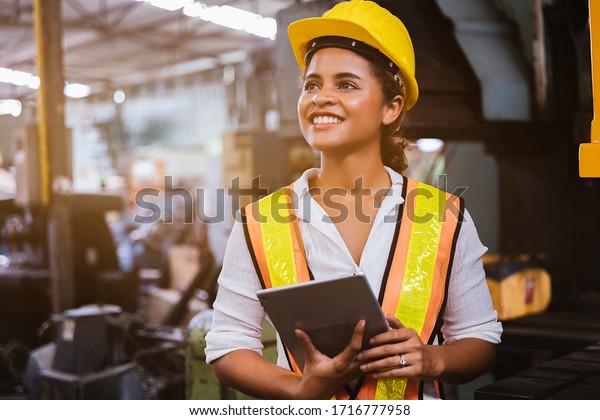 Industry maintenance engineer woman dark skin\
wearing uniform and safety helmet under inspection and checking\
production process on factory station by tablet. Industry,\
Engineer, construction\
concept.
