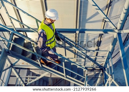 An industry worker descending the stairs on silo with tablet in hands.