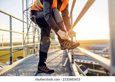 An industry worker tying shoelace on work shoes while standing on metal construction. - Shutterstock ID 2132483415