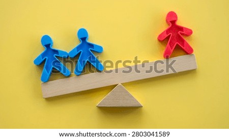 Inequality and leverage concept with two blue figures outweighed by a single red figure on a wooden seesaw