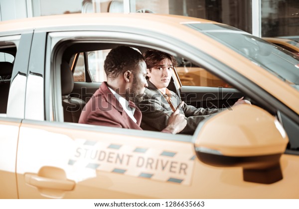 Inexperienced driver. Inexperienced\
young driver feeling worried sitting in the car near his\
teacher