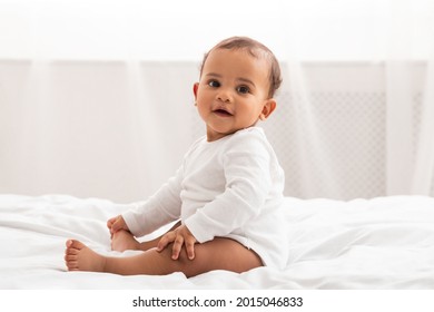 Infancy. Adorable African American Infant Baby Sitting In Bed Smiling To Camera At Home. Cute Toddler Boy Posing Wearing White Longsleeve Coverall In Bedroom Indoor. Babies Fashion And Clothes