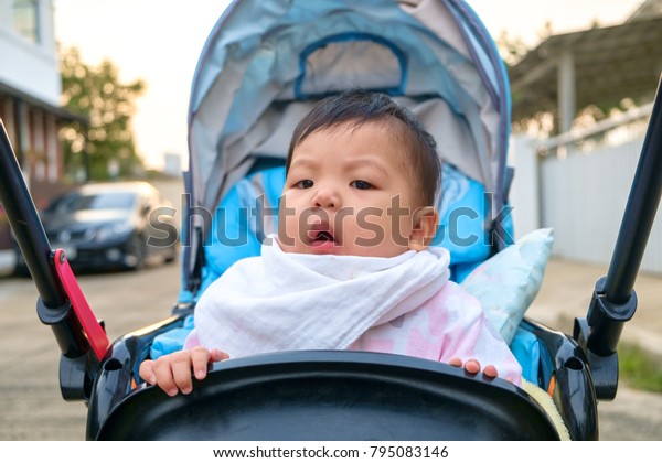 Infant 7 months sitting on the cart. There is a\
white scarf on a bright\
morning.