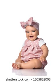Infant baby girl with opened mouth wearing polka dot dress and headband with bow sits on the floor looks at camera. Happy infancy and babyhood concept
