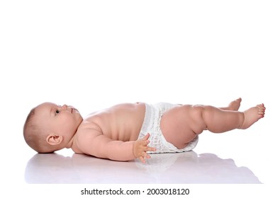 Infant child baby girl kid in diaper is lying on her back sideways to camera, looking up and holding her legs up isolated on a white background