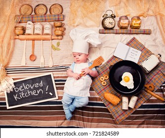 Infant cook baby boy portrait wearing apron and chef hat, prepare breakfast from fried egg. Textile decoration of a kitchen interior