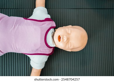 Infant CPR training dummy lying on a mat, used for teaching lifesaving techniques in first aid classes. Essential for healthcare and emergency response training. - Powered by Shutterstock