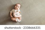 Infant lying on brown bed smiling with joy. Baby girl with delighted expression plays touching toes with hands and relaxing on bed, copyspace