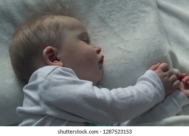 Infant to one year old blonde in white clothes is sleeping on a white bed, selective focus.