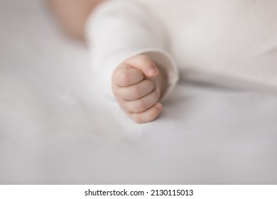 Infant Sleepy Baby Hand Wearing White Clothes, Sleeping On Bed, Resting On Pale Sheet, Soft Mattress. Arm Of Few Month Infant Boy Or Girl Lying In Beddings. Child Care, Bedtime Concept. Close Up