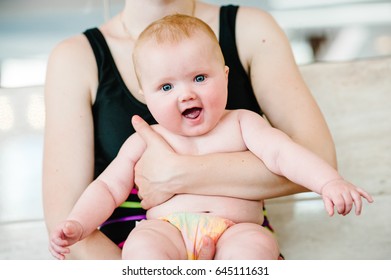 infant. Surprised. with an open mouth. red-head hair. close-up. mom holding baby girl 6 months, a baby in her arms at the pool. The first swimming lesson. Prepare to dive. baby in diapers