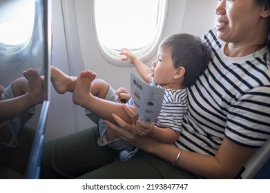 Infant traveling in airplane sitting on its mother lap using in flight entertainment screen. One year old baby boy flying in airplane and trying to entertain himself